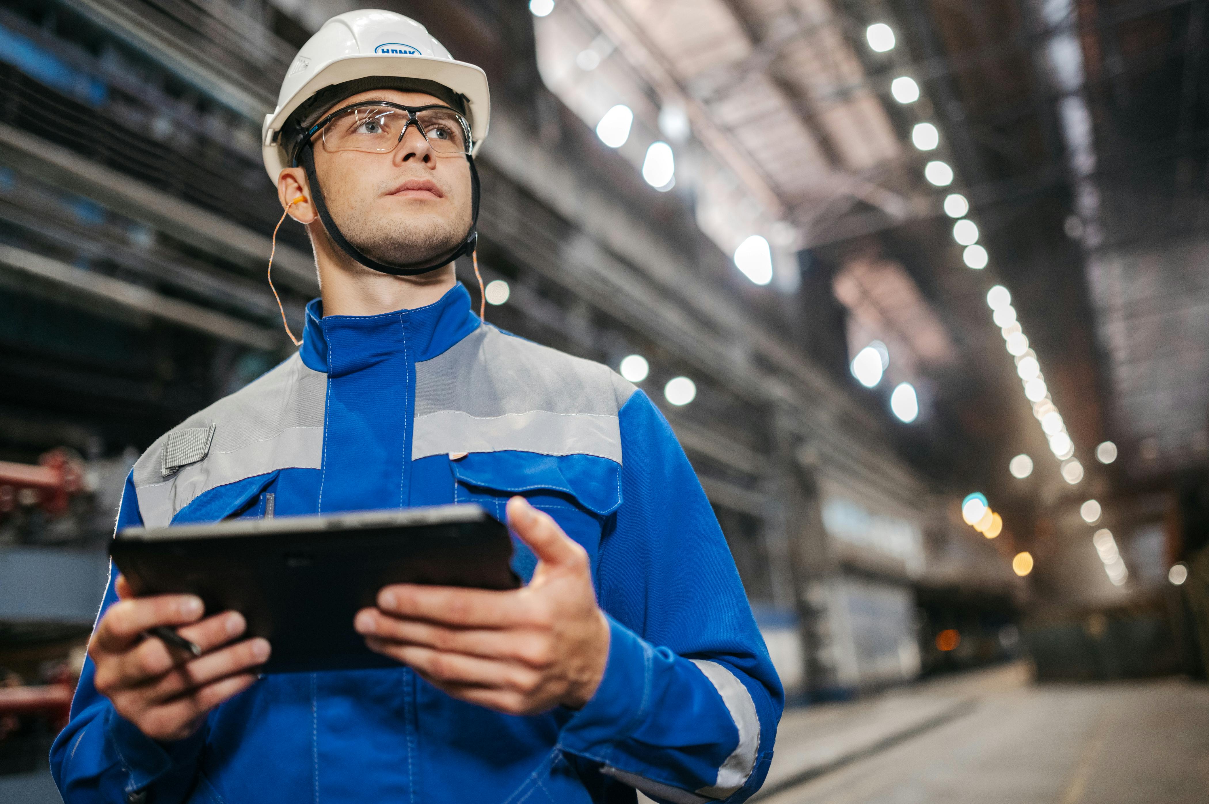 A factory worker in safety gear using a tablet to run workflows on industrial equipment