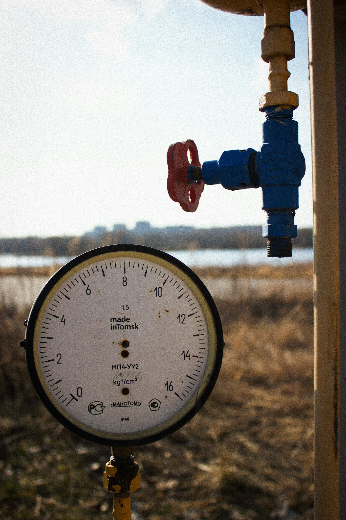 A weathered analog pressure gauge and valve mounted on a pipe in the field